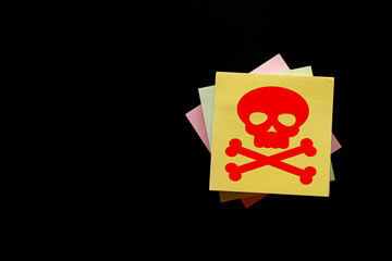 Caution Symbol with Red Skull on Yellow Sticky Note on Black Background: Representing Danger, Risk, and Hazard Awareness.