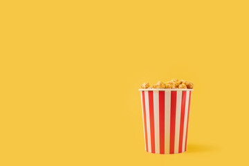 Popcorn bucket, striped box, caramel corn, tasty sweet snack, yellow background, copy space