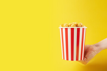 Hand with popcorn striped bucket, cinema film snack,salty grain, tasty pop corn