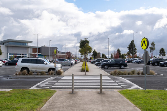 A crosswalk leads to a footpath in an outdoor parking lot outside a shopping center. The raised zebra crossing acts as a speed bump to slow down vehicles and protect pedestrians.