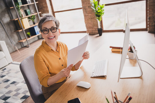 Photo of nice senior woman read report sit table dressed yellow formalwear executive business leader work in cozy beautiful office interior