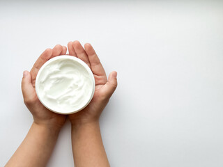 Close up of childs hands holding container of hand cream on white background with copy space. Skincare and moisturizing concept. Design for healthcare and wellness.