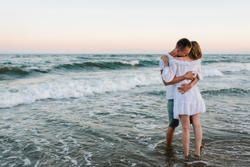 Couple in love hugging and kissing on seashore in sea. Male kisses and hugs female standing on...