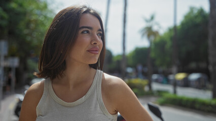 Beautiful young hispanic brunette woman standing outdoors on an urban street in a city setting,...