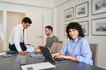 A woman is sitting at a desk with a laptop and a man is standing behind her