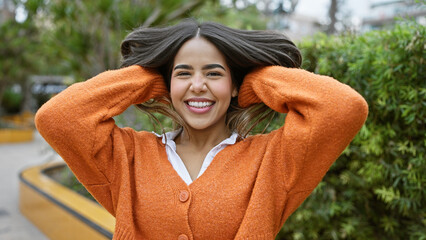 A cheerful young hispanic woman enjoys the outdoors, her vibrant smile complementing the green park...