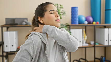 Obraz premium A young hispanic woman experiences neck pain in a rehabilitation clinic's therapy room.