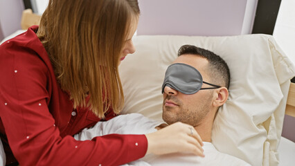 A woman caring for a man wearing a sleep mask in a bedroom, depicting intimacy and comfort in a domestic setting.