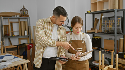 Woman and man reviewing notes together in a woodworking workshop, suggesting teamwork and carpentry skills.