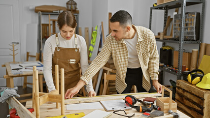 A man and woman work together in a well-equipped carpentry workshop, assembling a wooden structure.