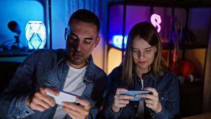 Man and woman focused on gaming with smartphones in a neon-lit home gaming room at night.