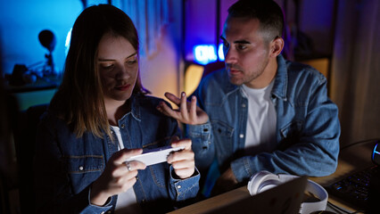 A man and woman engaged in gaming at night in a dark room, with intense concentration and modern technology