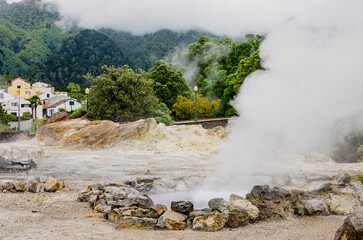 Smoke emanating from an active hot volcanic geyser against the background of green hills and a...