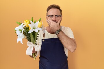 Middle age man with beard florist shop holding flowers shocked covering mouth with hands for...