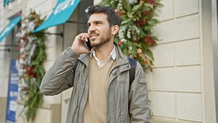 A young hispanic man with a beard, making a phone call on a busy urban street.