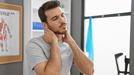 Hispanic man with beard feeling neck pain in a well-lit physiotherapy clinic's room