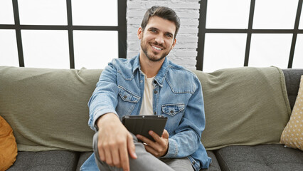 Handsome hispanic man smiling with tablet in a modern living room setting