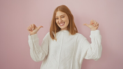 A cheerful young redhead woman in a white sweater pointing at herself with thumbs against a pink...