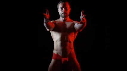Dark video of a young blonde bearded caucasian man dancing with red light in slow motion. Fashion trendy studio videoclip gogo dancer isolated with black background - Powered by Adobe