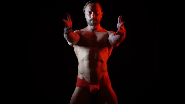 Dark video of a young blonde bearded caucasian man dancing with red light in slow motion. Fashion trendy studio videoclip gogo dancer isolated with black background