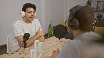 Two men in a podcasting studio with microphones and headphones having a friendly conversation.