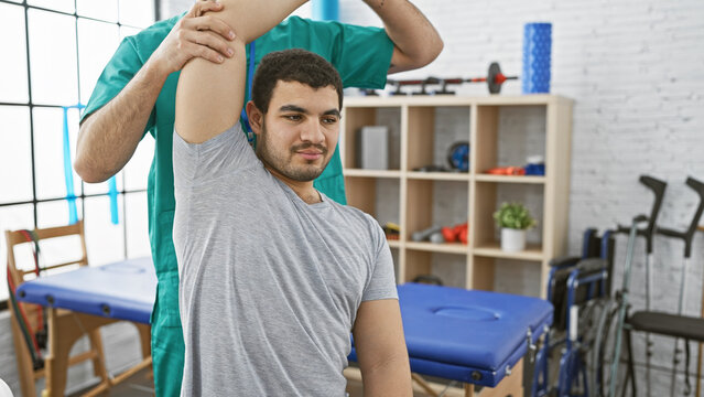 A physiotherapist assists a male patient with shoulder rehabilitation in a modern physiotherapy clinic.