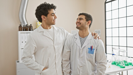 Obraz premium Two men in white lab coats bonding and smiling in a well-equipped modern laboratory.