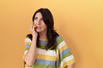 Middle age hispanic woman standing over yellow background looking stressed and nervous with hands...