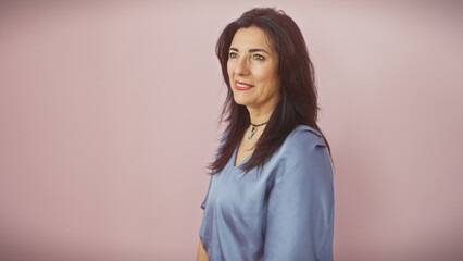 Fototapeta premium Mature hispanic woman in a blue blouse stands against a pink isolated background, exuding confidence and beauty.