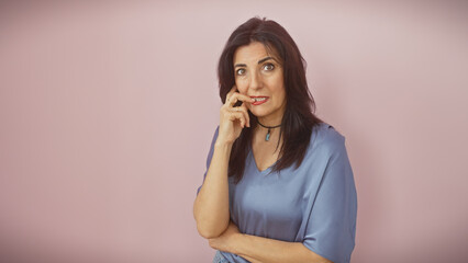 A pensive hispanic middle-aged woman stands against a pink background, exuding a sense of maturity...