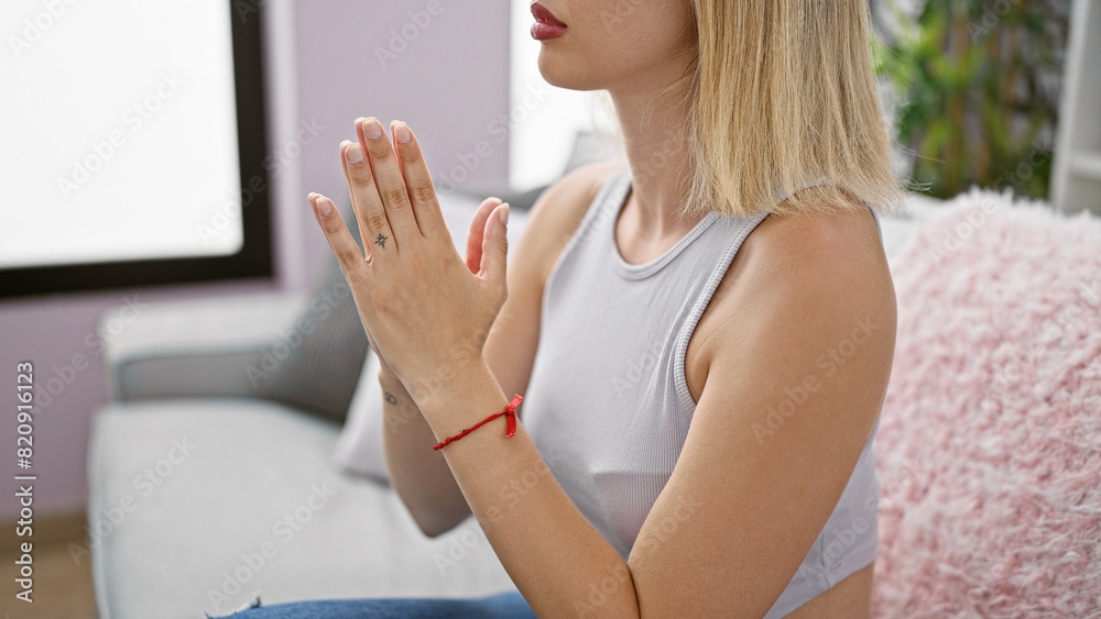 Canvas Prints Young blonde woman praying with closed eyes sitting on sofa at home