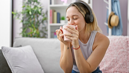 Young blonde woman listening to music drinking coffee smiling at home