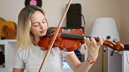 Young blonde woman musician playing violin at music studio