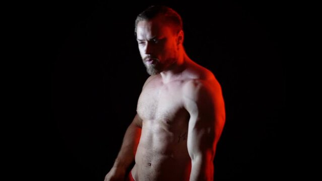 Dark video of a young blonde bearded caucasian man dancing with red light in slow motion. Fashion trendy studio videoclip gogo dancer isolated with black background