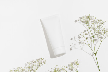 White mockup tube of natural face or body cream on white isolated background with flowers. The...