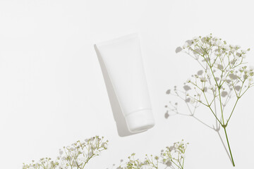 White mockup tube of natural face or body cream on white isolated background with flowers. The concept of skin care cosmetics, moisturizing and nutrition