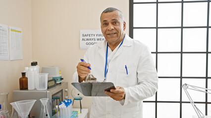 A confident middle-aged hispanic man in a white lab coat analyzes a clipboard in a well-lit...