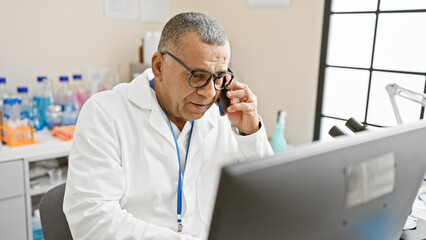 Concentrated hispanic man wearing glasses and lab coat analyzing data on a computer screen in a...