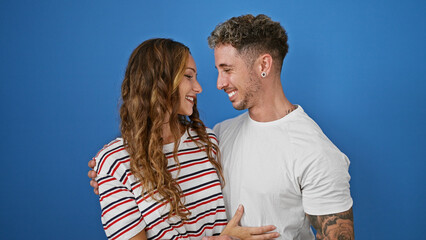 Affectionate couple laughing together against a solid blue background, depicting love and happiness.