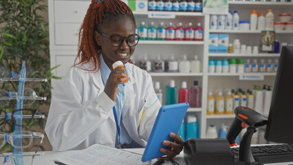 African female pharmacist using a tablet inside a well-stocked pharmacy.