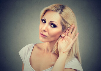 Woman holds her hand near ear and listens carefully isolated on gray wall background