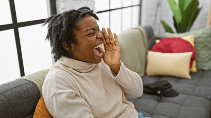 A cheerful woman with dreadlocks shouting indoors while sitting on a sofa in a cozy living room.