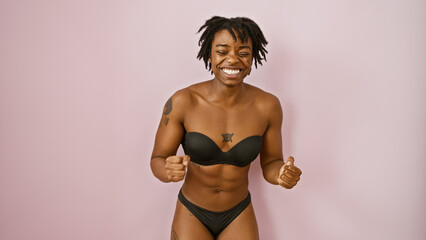 A joyful young african american woman with dreadlocks posing in underwear against a pink isolated background.