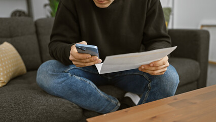 Hispanic man using smartphone and reading paper in a cozy living room setting
