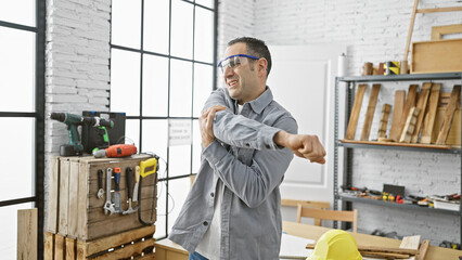 Hispanic man stretching in a bright carpentry workshop with tools