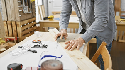 Young man sanding wood in a well-equipped carpentry workshop, showcasing skill and craftsmanship.