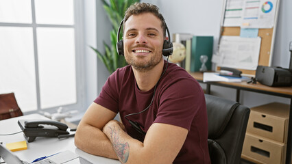 Handsome young man with a beard wearing a headset smiling in a modern office setting.