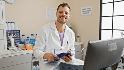 Handsome hispanic man with beard in a clinic wearing lab coat holding clipboard smiling at camera