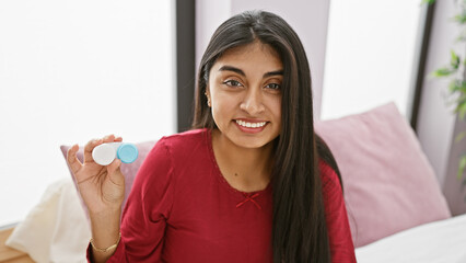 Smiling south asian woman holding a contact lens case in a modern bedroom