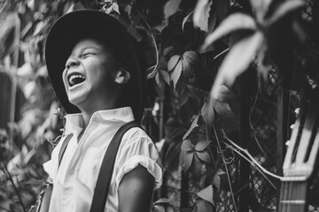 a little guitarist in a hat stands by an iron fence entwined with ivy and laughs merrily